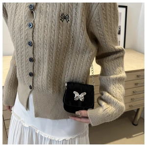 Close-up of a black mini saddle bag with silver butterfly buckle on a beige sweater