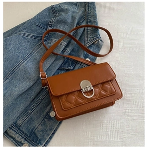Macro detail of brown quilted faux leather flap with silver metal lock on small crossbody bag
