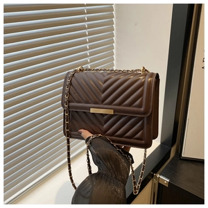 Detail of dark brown chain bag featuring V-shaped quilting and gold metal hardware