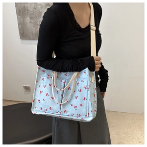 Detail of light blue canvas tote bag with cherry print and adjustable cream shoulder strap