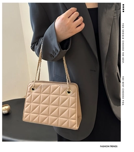 Close-up of beige quilted shoulder bag with gold chain strap worn over a grey blazer