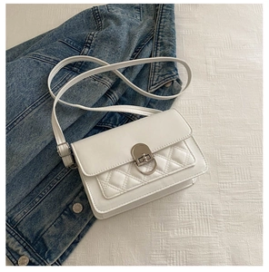 Detail of white quilted crossbody bag with silver oval twist lock on denim jacket