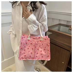 Close-up of pink canvas tote bag with red cherry print and functional front pockets