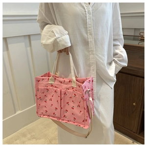 Detail of pink floral nylon tote bag with cherry pattern, front pockets, and adjustable strap