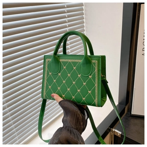 Detail of green quilted crossbody bag with small gold heart embroidery and twin handles