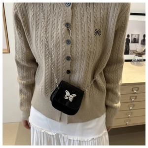 Close-up of a mini black crossbody saddle bag with a silver butterfly buckle and chain