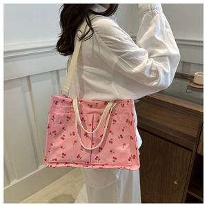 Pink tote bag detail with red cherry print, adjustable shoulder strap, and front pockets