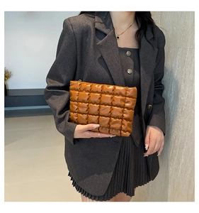 Gros plan sur la pochette matelassée caramel portée par un mannequin en costume gris