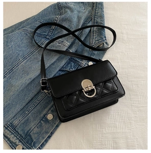 Detail of black quilted crossbody bag with silver oval twist lock on denim background