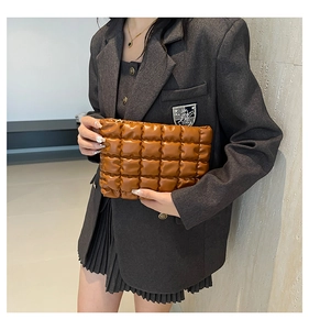 Pochette matelassée en cuir marron tenue par un mannequin en blazer gris et jupe plissée