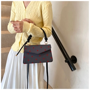 Close-up of gray crossbody bag with red polka dots and a black knotted handle strap