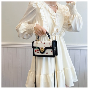 Close-up of cream crossbody bag with cherry print and golden flower clasp detail