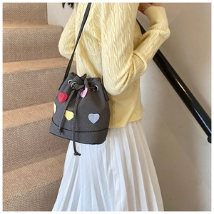 Dettaglio borsa a secchiello grigia con toppe a cuore colorate su outfit casual