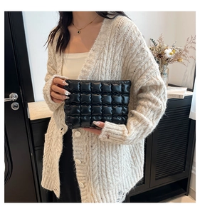 Détail d'une pochette matelassée noire brillante tenue par un mannequin en maille