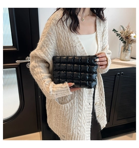 Gros plan d'une pochette matelassée en cuir PU noir tenue par un mannequin en intérieur