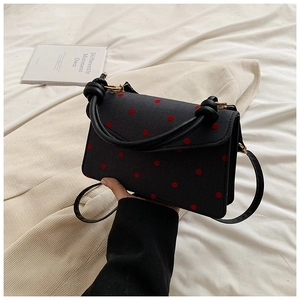 Detail of a dark square crossbody bag with red polka dots and golden hardware accents