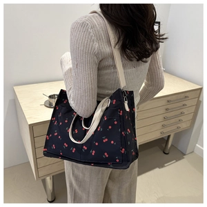 Detail of cherry print canvas tote bag featuring front pocket and woven shoulder strap