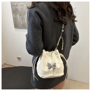 Détail du sac seau blanc à cordon avec une grande boucle papillon en métal liquide argenté