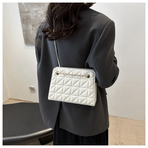 Detail of white quilted leather chain bag worn on shoulder with a grey office blazer
