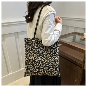 Close-up of leopard print canvas tote bag with black slim straps in a minimalist setting