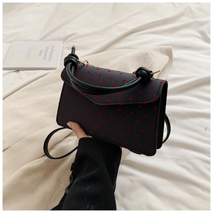 Detail of dark crossbody bag with red heart pattern, knot handle and gold hardware