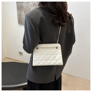 Detail of white quilted chain bag with gold hardware worn on a grey blazer jacket