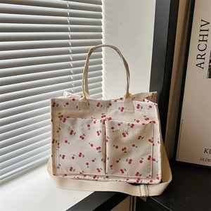 Large cherry print canvas tote bag with front pockets and adjustable strap in room setting