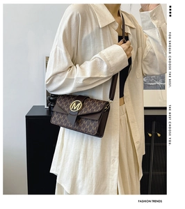 Detailed close-up of brown crossbody bag with gold M buckle and logo pattern
