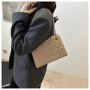 Close-up of beige quilted crossbody bag with gold chain strap on a model's shoulder