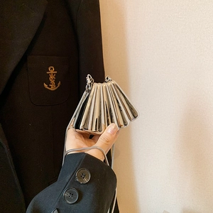 Silver metallic shell-shaped crossbody bag with a chain strap held against a black suit