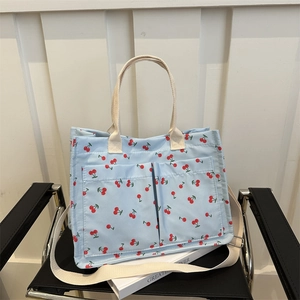 Light blue canvas tote bag with red cherry print and adjustable strap on a chair
