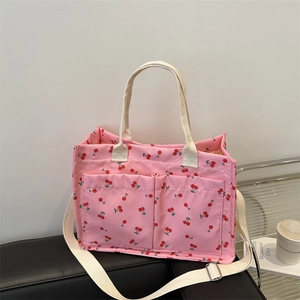 Pink canvas tote bag with red cherry print featuring front pockets and adjustable strap