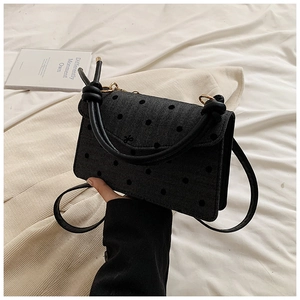 Detail of black polka dot handbag featuring a knotted handle and small bow accent