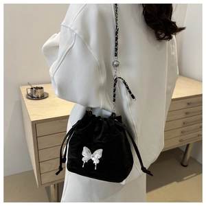 Détail du sac seau noir en velours avec papillon en métal argenté porté par le mannequin