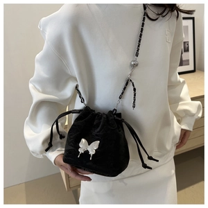 Détail macro du sac seau en velours noir avec boucle papillon argentée et bandoulière chaîne