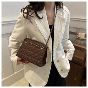 Close-up of brown quilted chain tote bag worn over a stylish white suit jacket