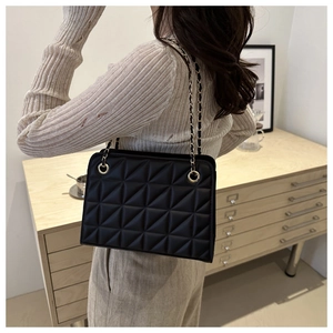 Detail of black quilted tote bag with geometric pattern and gold chain strap worn by model