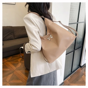 Dettaglio della borsa tote beige lucida con fiocco in metallo argento e tracolla regolabile