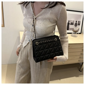Close-up of black quilted shoulder bag with gold chain strap worn by a model
