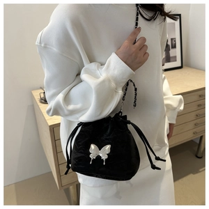 Détail d'un sac seau noir avec papillon argenté et bandoulière chaîne porté par un mannequin