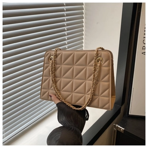 Detail of quilted beige square shoulder bag with golden chain strap in sunlight