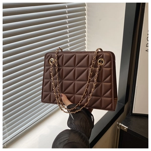 Detail of dark brown quilted crossbody bag with gold chain strap on window background