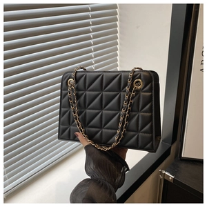Detail of black quilted square shoulder bag with gold chain strap and faux leather texture
