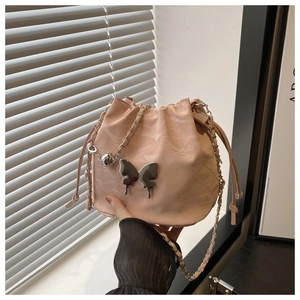 Détail du sac seau rose clair avec emblème papillon argenté et bandoulière chaîne