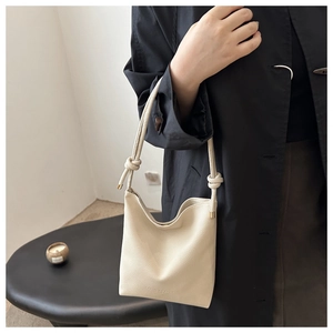 Detail view of a creamy white litchi pattern leather bucket bag with tied rope straps