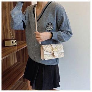 Detail of cream crossbody bag with M-letter print and gold buckle on a model
