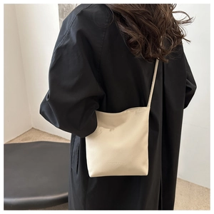 Detail of cream pebbled leather phone bag with embossed fashion text and slim strap