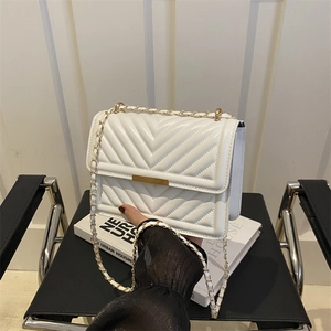 White chevron quilted crossbody bag with gold chain strap shown on black chair display