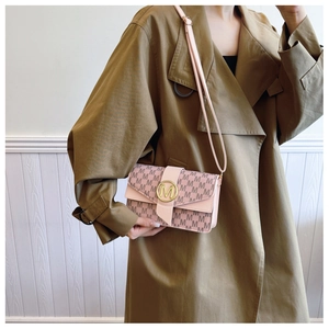 Detail of monogram patterned shoulder bag with gold metal lock on beige trench coat