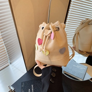 Elegante borsa a secchiello in paglia beige con toppe a cuore colorate e chiusura a cordoncino